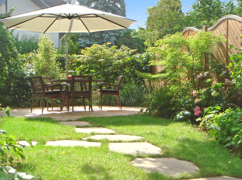 Der Blick in den Garten: der runde Sitzplatz aus Natursteinplatten ist der zentrale Blickfang.